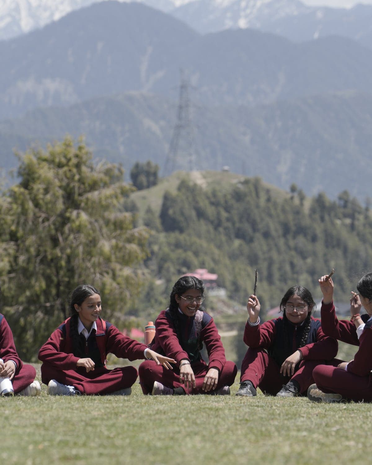 Boarders sitting together on the grass below the Himalayan peaks